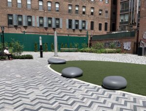 View of Manuel Plaza, an open space with grey herringbone bricks paving the ground and a circular area of astroturf at the center.